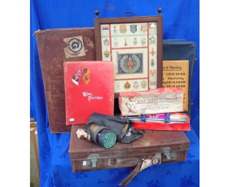 A FIRESCREEN DECORATED WITH CIGARETTE SILKS a WWI scrapbook, a gas mask, Ajax chest expanders, old suitcases, and a shop open