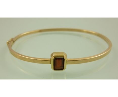 A GOLD COLOURED METAL BANGLE set with a single garnet