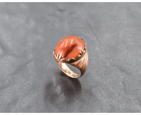 An oriental rose gold ring having an oval carnelian cabouchon in a decorative collared and claw mount to moulded sholders on 