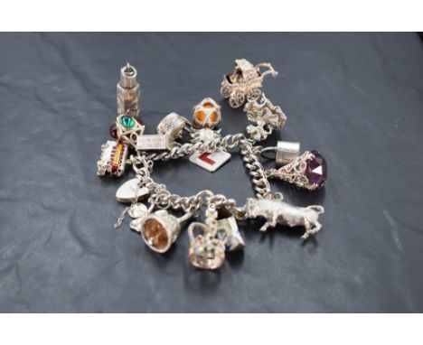 A silver and white metal charm bracelet, the curb type links suspending a variety of charms, including lantern, bull, crown, 