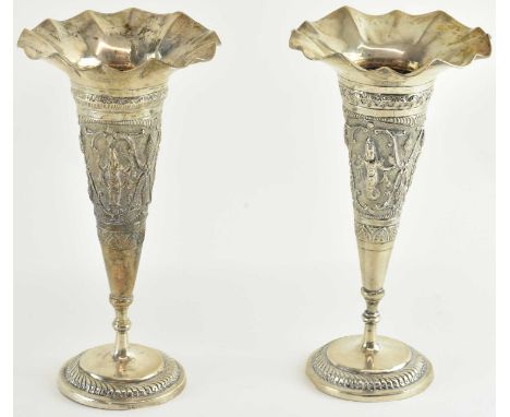 A pair of Indian white metal trumpet vases, both with wavy rims and decorated with figures amongst flora, both height 15.5cm,