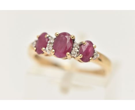 A 9CT GOLD RUBY AND DIAMOND RING, designed with a row of three oval cut rubies, each in a four claw setting, with six single 