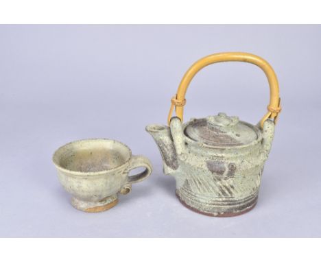 IAN GODFREY (1942-1992); a stoneware teapot with cane handle, height 11.5cm (excluding handle) and a cup, made circa 1970s (2