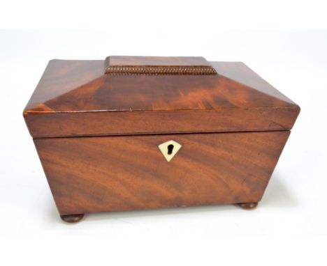 An early Victorian mahogany sarcophagus tea caddy with two sections, both with lids, with lozenge shaped escutcheon and on bu