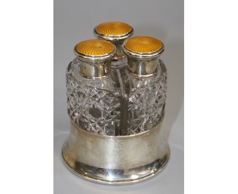 A set of three silver mounted cut glass scent bottles, each with mustard guilloche enamel screw cap fitted in a silver coaste