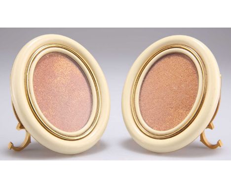 CARTIER - A PAIR OF GILT METAL AND ENAMEL PHOTOGRAPH FRAMES oval form in cream enamel and gilt, on strut stands with twin 'C'