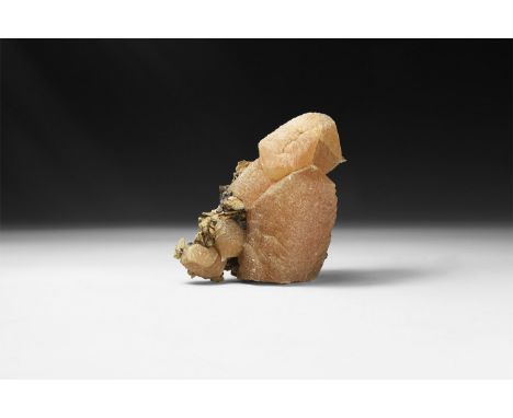 A large brown calcite crystal with mottled surface and clusters of smaller calcite crystals to the side; to the base sheets o