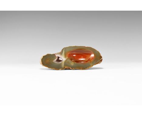 A finely cut and polished thick agate slice with variegated grey and red bands; right side cut with an elliptical bowl shape,