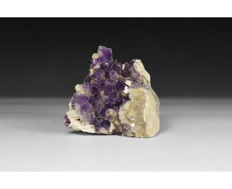 A fine specimen of purple cubic fluorite crystals on a matrix with crystals of barite, in white card tray with label reading: