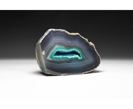 A fine cut and polished agate geode half with bands of pale grey and central green band surrounding cavity filled with miniat
