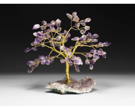 A gemstone tree consisting of a brass trunk and branches tipped with polished amethysts, mounted on a section of amethyst geo