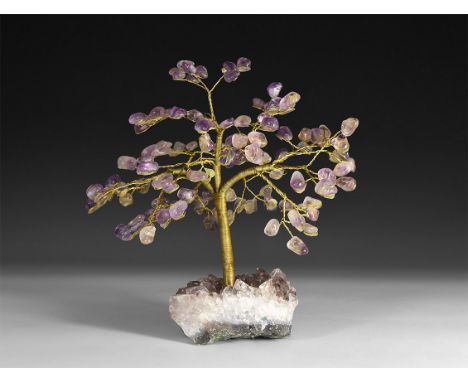 A gemstone tree consisting of a brass trunk and branches tipped with polished amethysts, mounted on a section of amethyst geo