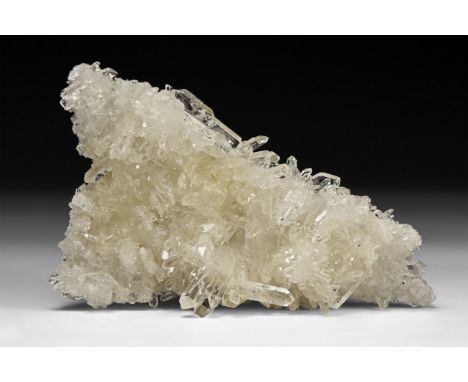 A fine specimen of transparent quartz crystals formation on a matrix, in white card tray with label reading: 'Quartz, Corinto