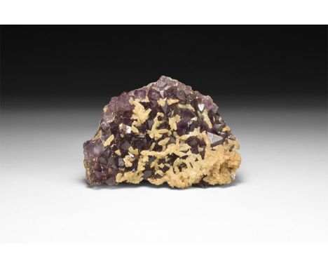 A fine specimen of a deep purple amethyst crystals on a matrix, with smaller calcite crystals overgrown to the centre and one