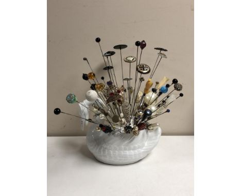 A collection of nearly one hundred stick pins and hat pins, some silver examples, in a ceramic swan display