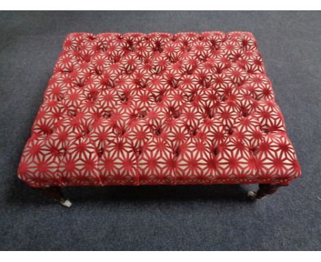 An oversized foot stool re-upholstered in a red and cream fabric on ceramic casters.  