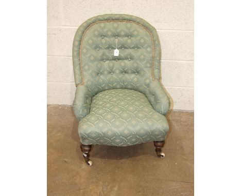 A Victorian button-back upholstered low tub chair on turned legs with casters.