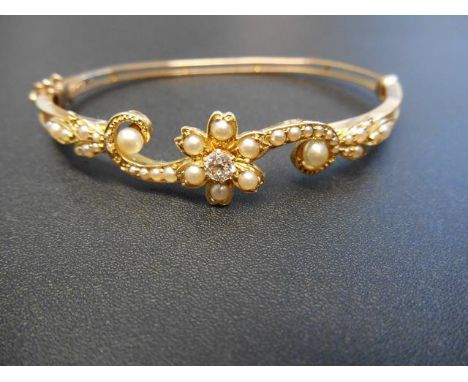 A yellow metal hinged bangle with diamond and seed pearls in floral setting, with safety chain, approx total gross weight 11.
