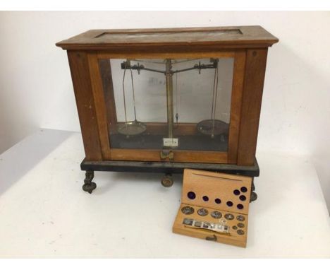 An Edwardian set of scales in glass case and adjustable base together with a set of weights bearing label Sold by AH Baird, E