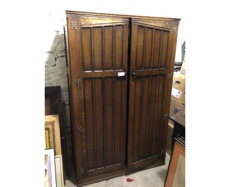 An oak wardrobe with dentil cornice above a pair of inset panel doors enclosing a plain interior, on plinth base (186cm x 120