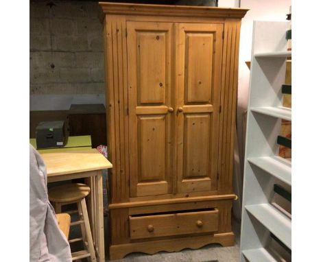 A modern pine wardrobe, the moulded cornice above a pair of inset panel doors, above a single drawer, raised on shaped plinth