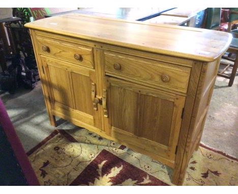 An Ercol light elm sideboard, the moulded rectangular top above a pair of frieze drawers and two panelled cupboard doors encl