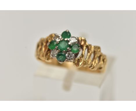 A YELLOW METAL GEM SET CLUSTER RING, flower cluster set with circular cut emeralds and diamonds, textured open work shoulders