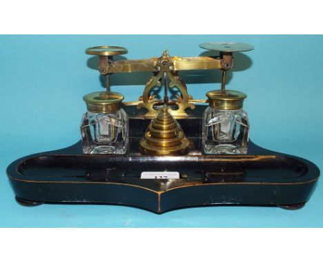 An ebonised desk stand, with a set of brass scales, weights, and a pair of glass inkwells, 30.5 cm wide