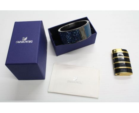 Yves Saint Lauren YSL black enamel and gold tone banded cigarette lighter, together with a Swarovski bangle, blue crystal dia