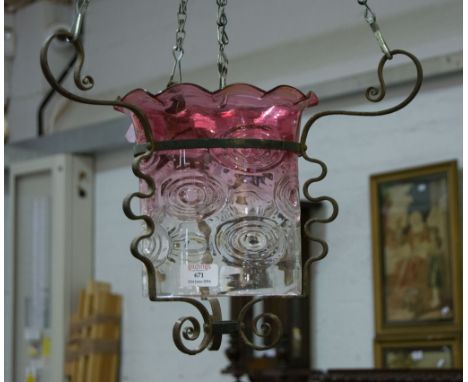 Wrought iron hanging light fitting with three chains supporting a glass shade in cranberry and clear glass.