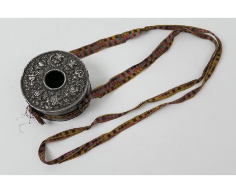 Tibetan silvered copper ghao/prayer box pendant, worked with Buddhist symbols, suspended from coloured sash, 11cm diameter 
