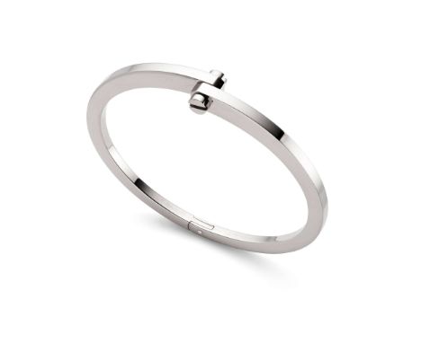  Cartier: A white gold 'Menotte' bangle  The 18 carat white gold tapered bangle, hinged at the base and connected centrally b