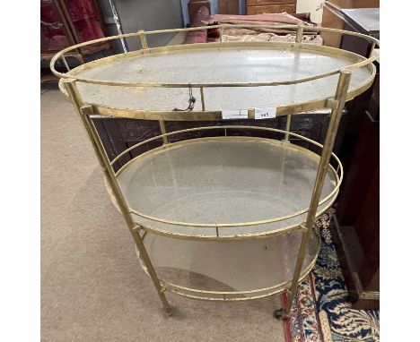 An early 20th Century oval metal framed three tier drinks trolley, 77cm wide, 107cm high, glass to bottom shelf damaged, meta