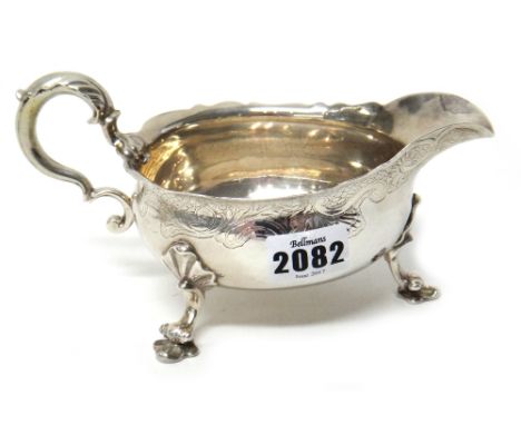 A George II silver sauceboat, with a shaped rim, scrolling handle, engraved decoration to the body and raised on three decora