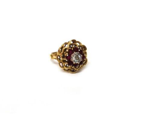 A gold, diamond and ruby nine stone cluster ring, pierced in an abstract design, mounted with the cushion shaped diamond at t