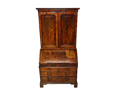 A George II feather banded figured walnut bureau cabinet, the pair of upper doors over a stepped and welled interior of two s