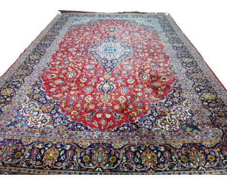 A Kashan carpet, Persian, the madder field with an ivory and indigo medallion, matching spandrels, all with floral sprays, an