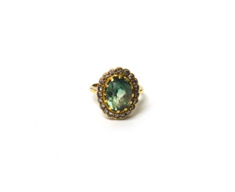 A gold, pale green tourmaline and diamond set oval cluster ring, claw set with the oval cut pale green tourmaline at the cent