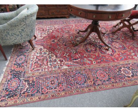 An Heriz carpet, Persian, the madder field with a bold indigo rosette medallion, ivory spandrels, all with floral sprays, a b