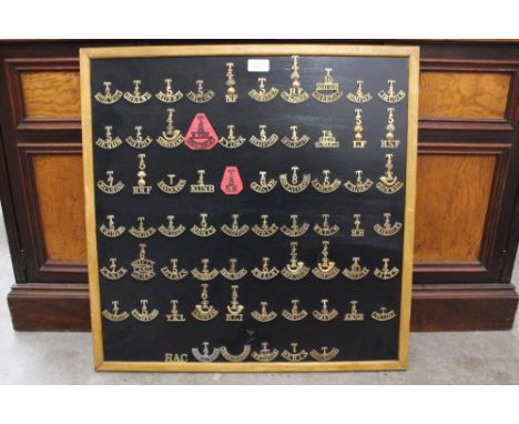 A framed board of WW1 British Army brass shoulder titles all from Territorial units. 66 in total.