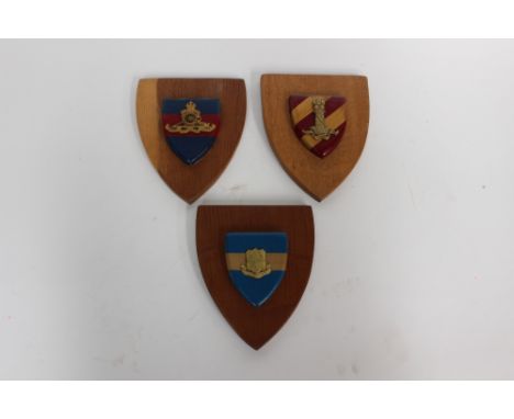 Three British Army wall plaques: each with separately applied metal badges on Corps coloured backgrounds upon a wooden sheild