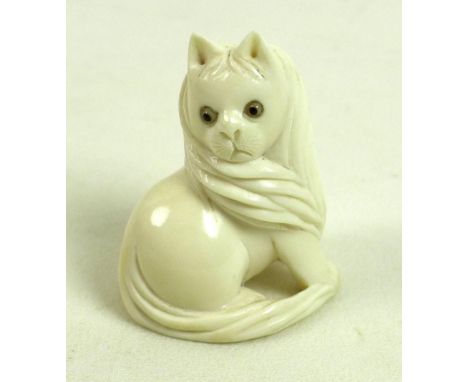 A Japanese ivory netsuke, Meiji period, circa 1900, carved as a cat sitting looking over it's right shoulder, with inset glas