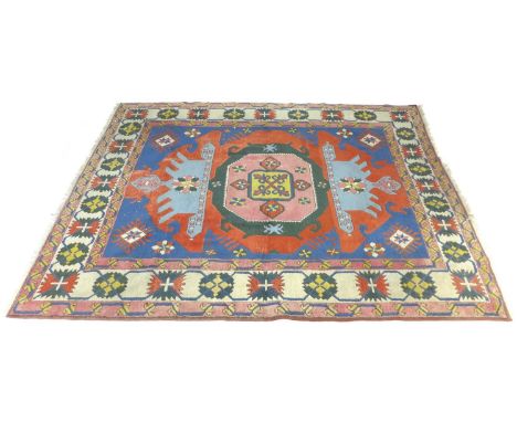 A Persian rug with blue ground, with oversized red, light blue, dark green, yellow, and white medallion to centre, wide styli