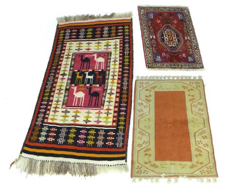 A group of three small rugs, comprising a flat weave rug with seven camels to the red, cream, and black field, surrounded by 