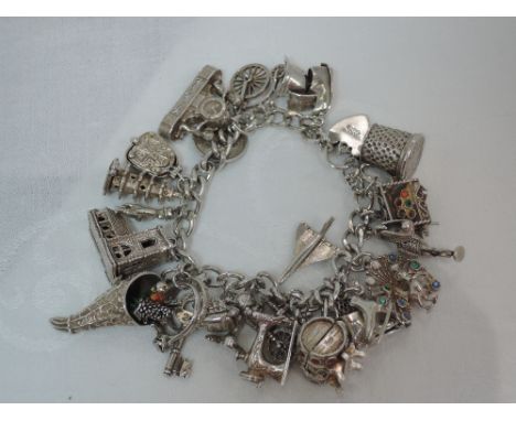 A white metal charm bracelet stamped silver having 25 charms including Concorde, peacock, church, scales etc