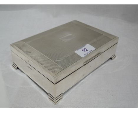 A silver cigarette box of rectangular form having engine turned decoration, plain cartouche and bracket feet, Sheffield 1964,
