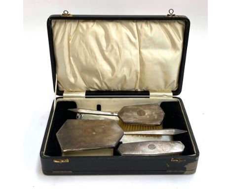 An engine turned silver cased dressing table set comprising clothes brush, hairbrush, and looking glass