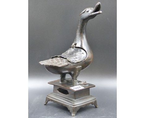 A CHINESE BRONZE DUCK CENSER STANDING ON A PLINTH WITH FOUR BRACKET LEGS, IT'S OPEN BEAK TURNED TO THE RIGHT, IT'S BACK WITH 