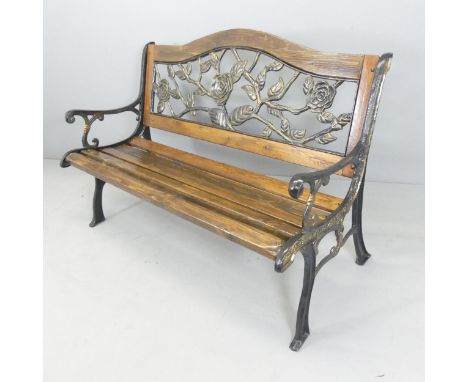 A pine slatted garden bench with cast iron ends and painted metal floral-design back panel. 130x89x65cm.