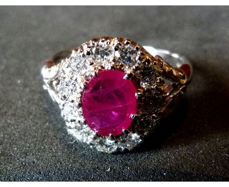 An 18ct. White Gold Ruby and Diamond Cluster Ring, with a central oval ruby surrounded by diamonds within a pierced shaped se